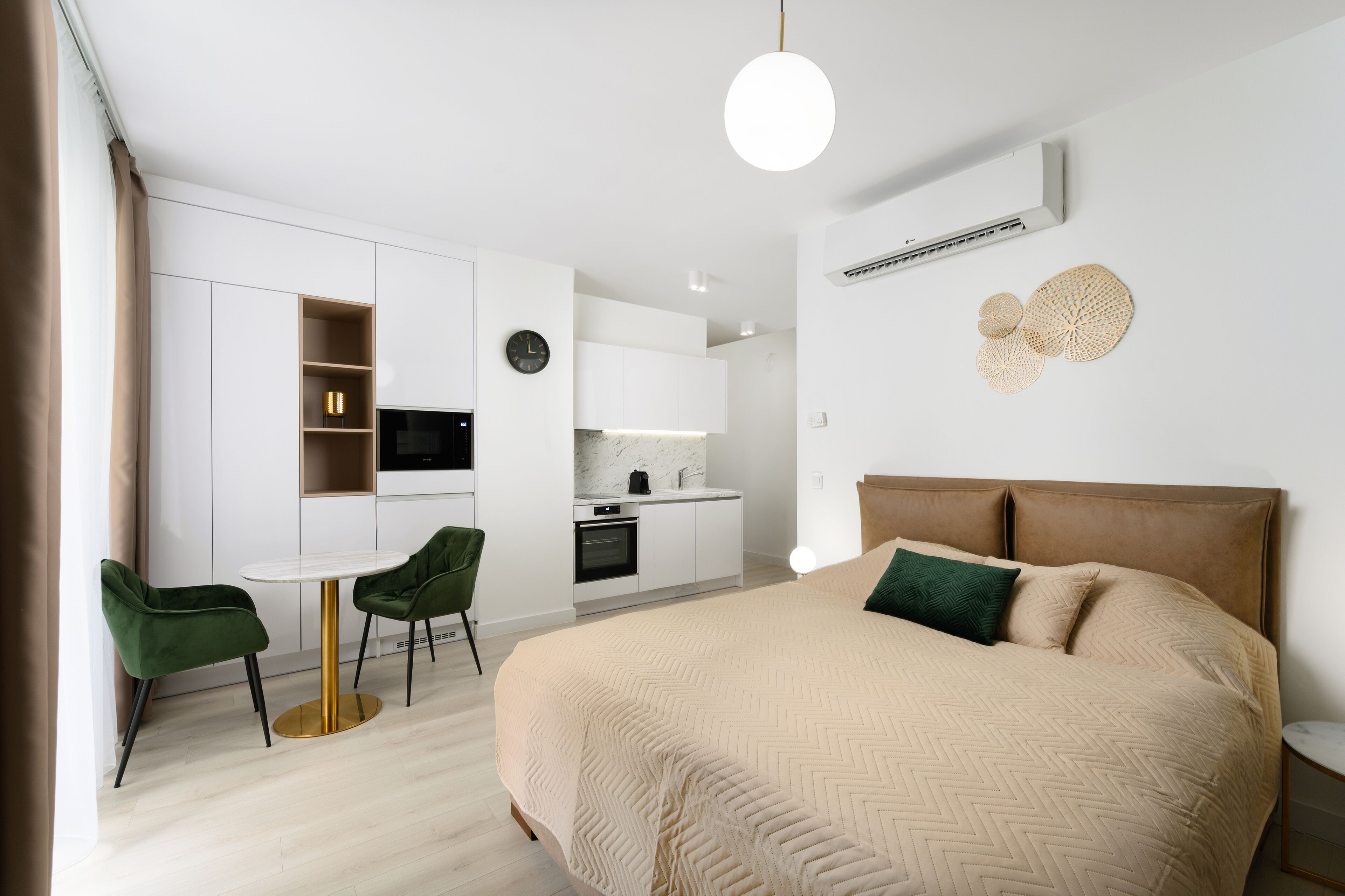 Een moderne hotelkamer met een groot bed, een zithoek met een ronde tafel en stoelen, een kitchenette en een groot raam.
