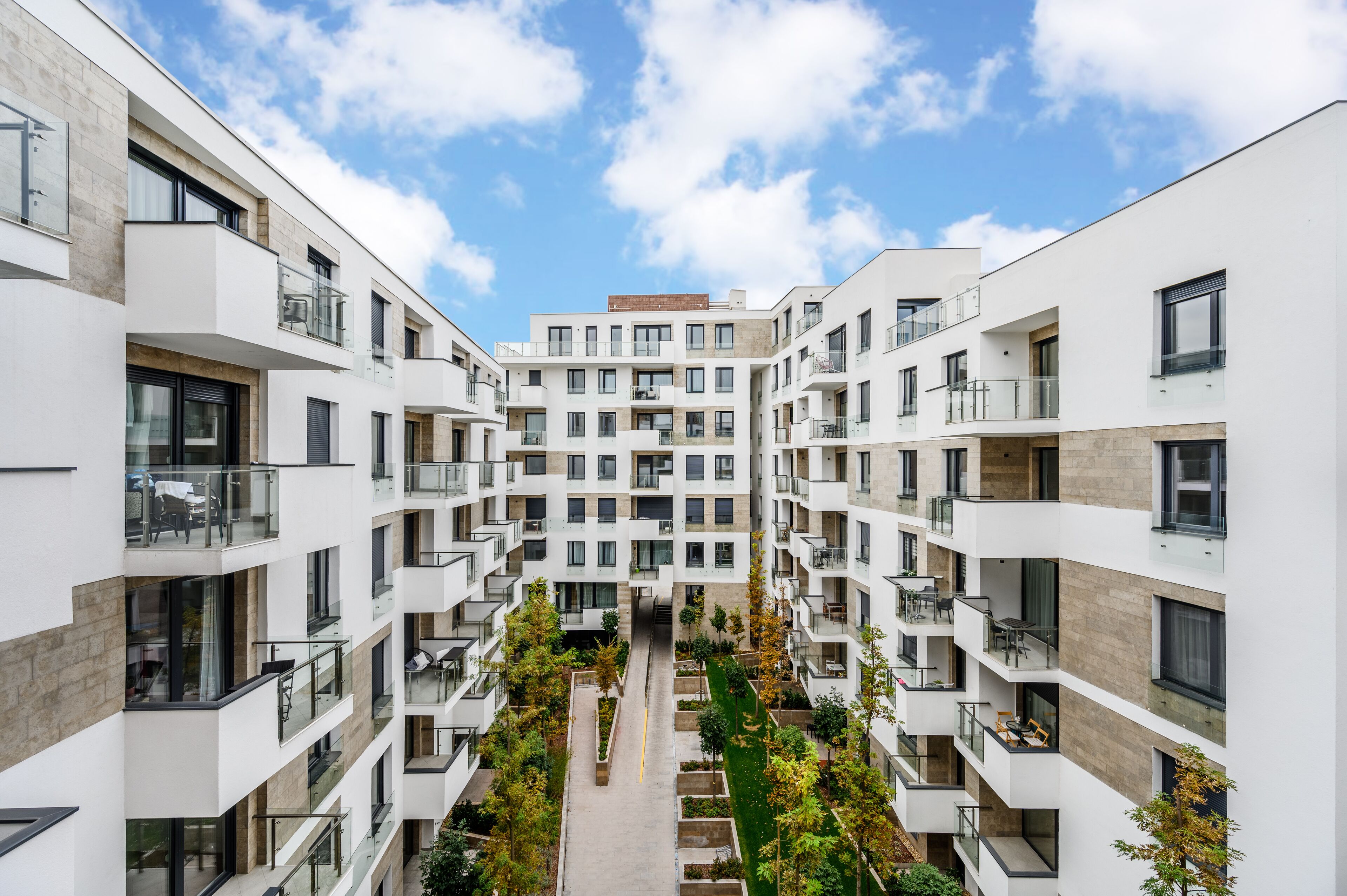 A modern multi-story residential building with balconies, a central courtyard, and a clear sky.