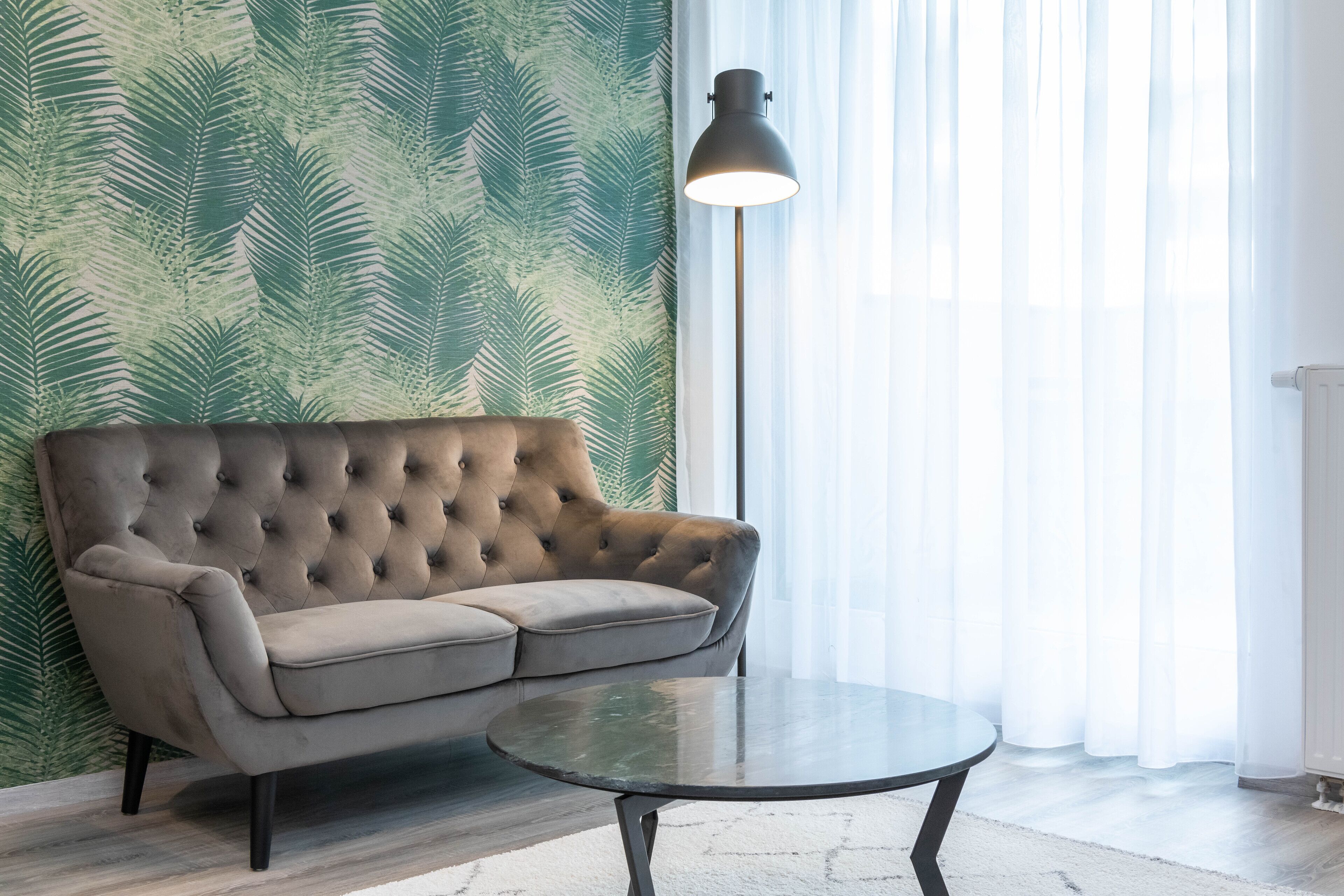 A room with a tufted sofa, a round glass table, and a floor lamp.