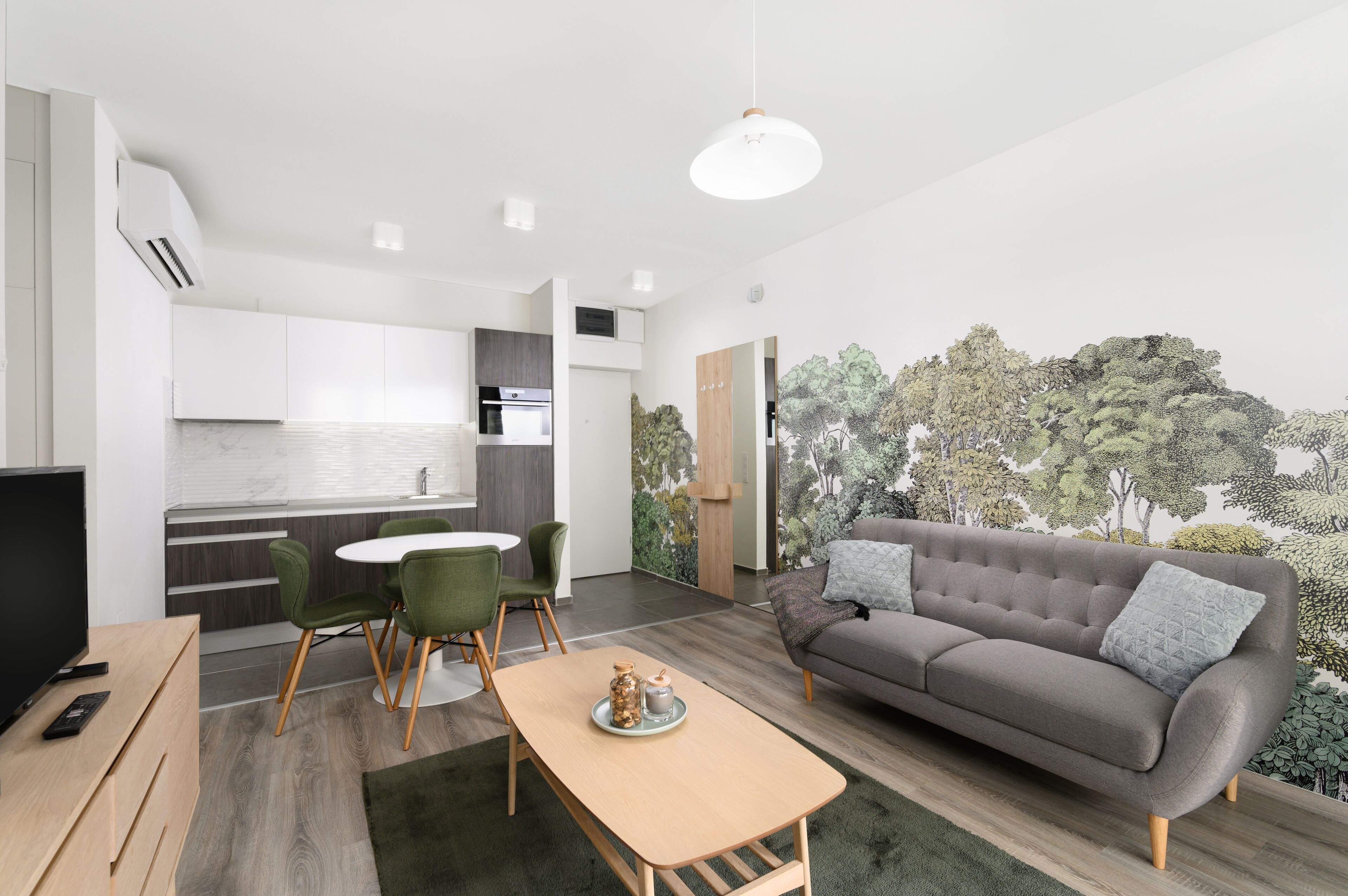 Un salon moderne avec un canapé gris, des fauteuils verts, une table basse en bois et un meuble pour la télévision.