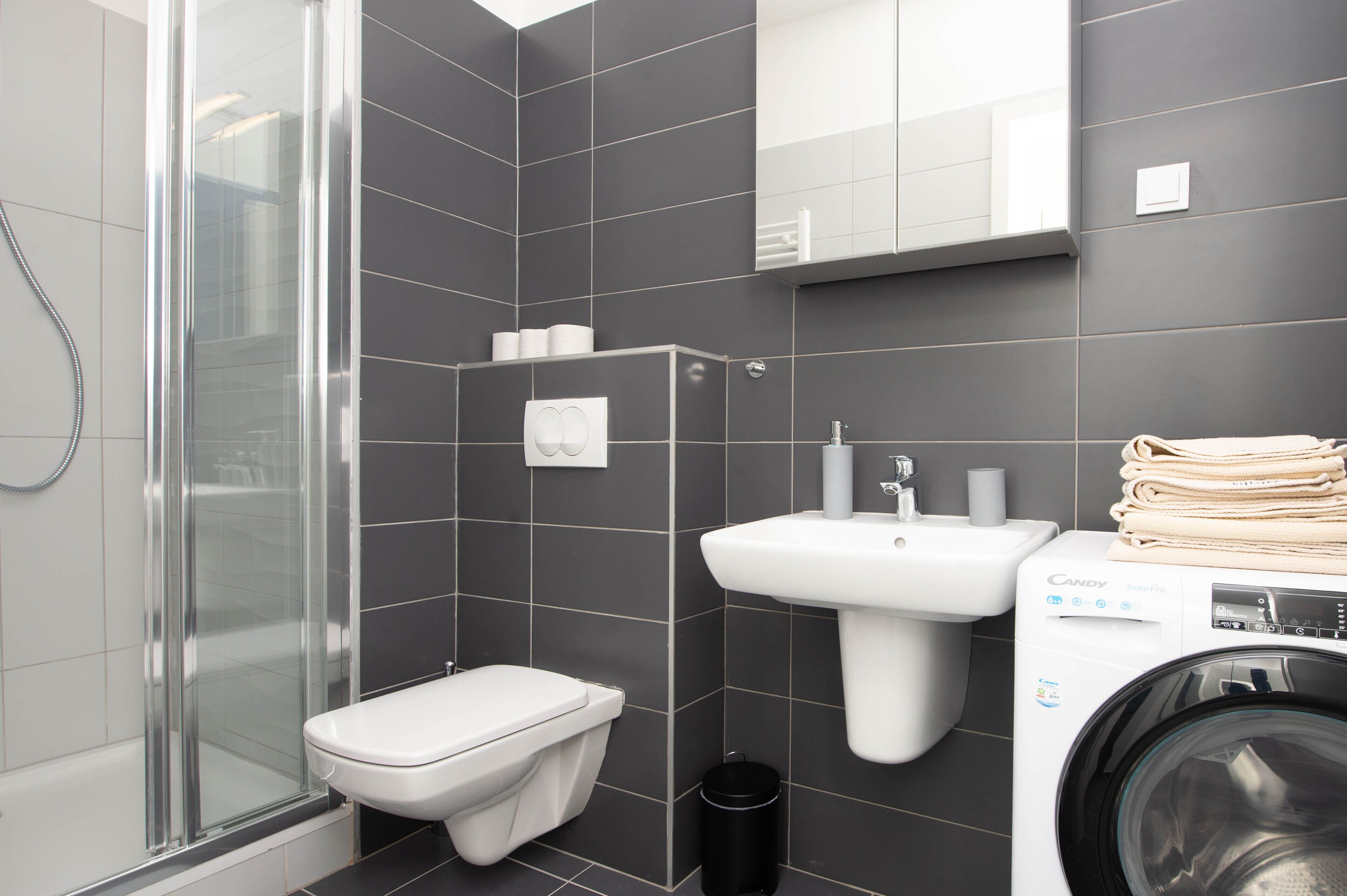 Un baño moderno con ducha de vidrio, inodoro, lavamanos y lavadora.