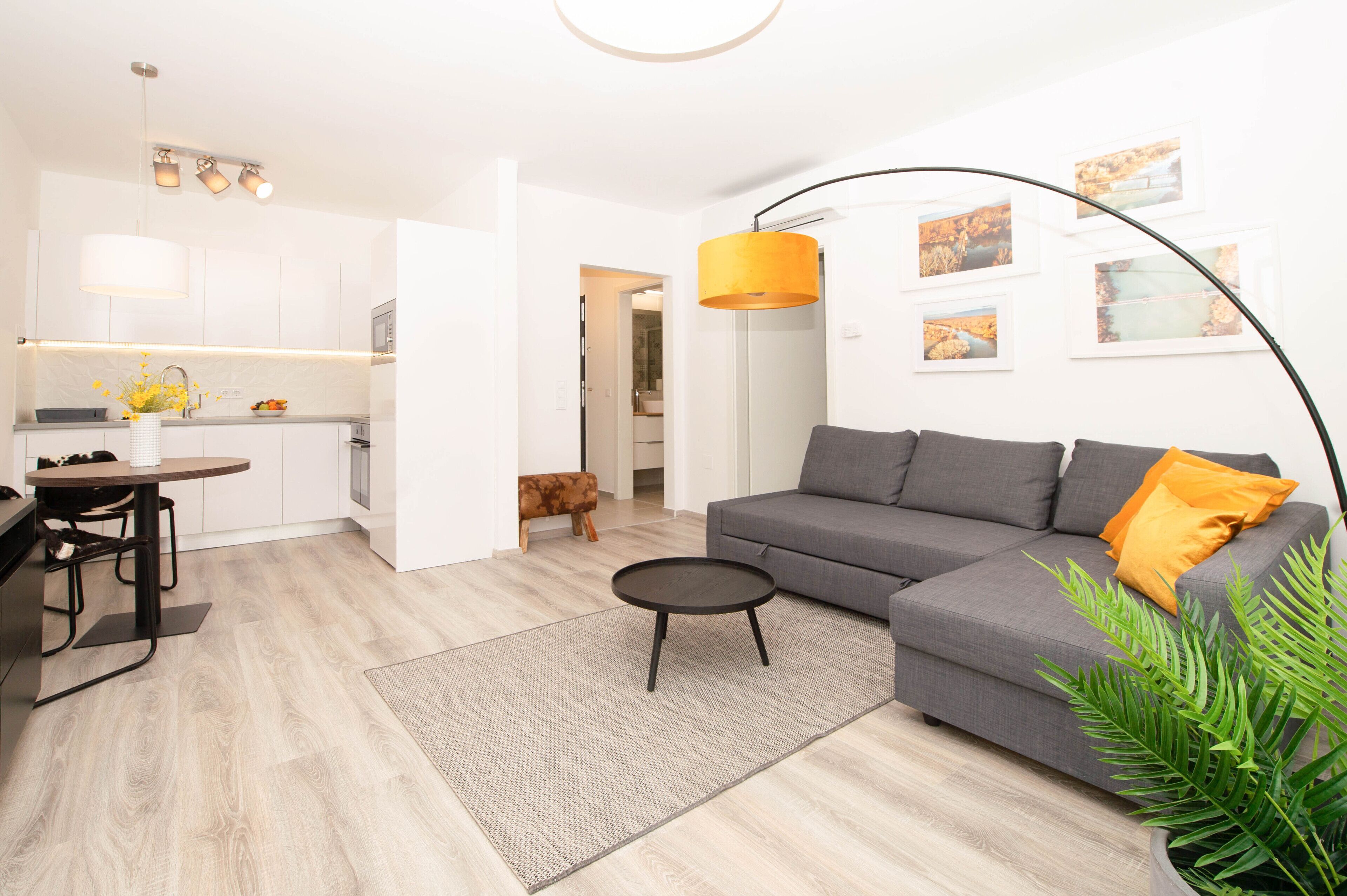 Ein modernes Wohnzimmer mit einem grauen Sofa, einem runden Couchtisch und einem Essbereich mit Tisch und Stühlen.