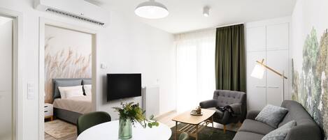 Una camera d'albergo moderna con un letto, una TV, un tavolo da pranzo con sedie, un divano e un quadro appeso al muro.