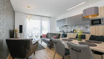 Een moderne keuken met grijze kastjes, een magnetron en een eethoek met een tafel en stoelen.