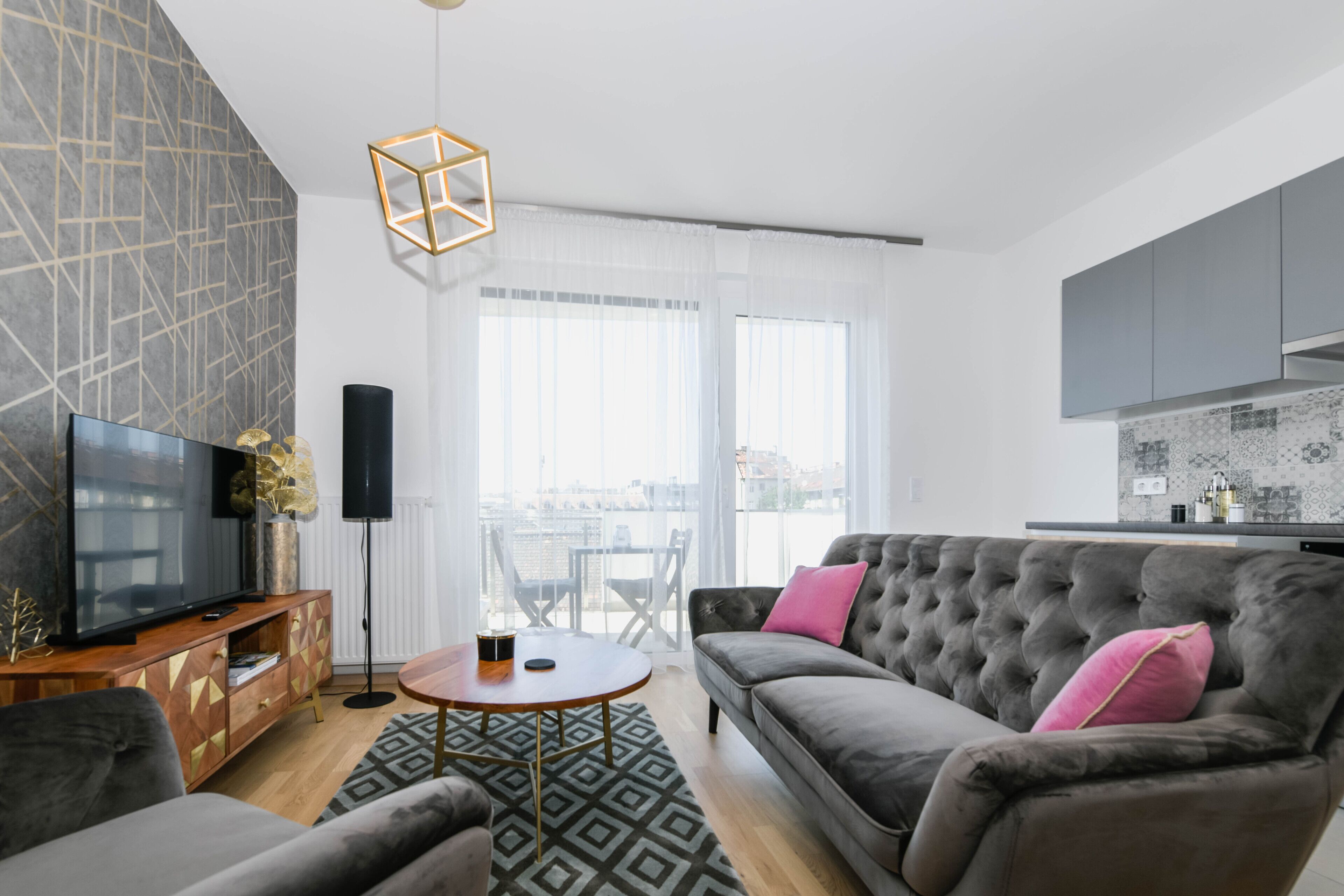 Een moderne woonkamer met een grijze bank, een houten salontafel en een grote flatscreen televisie.