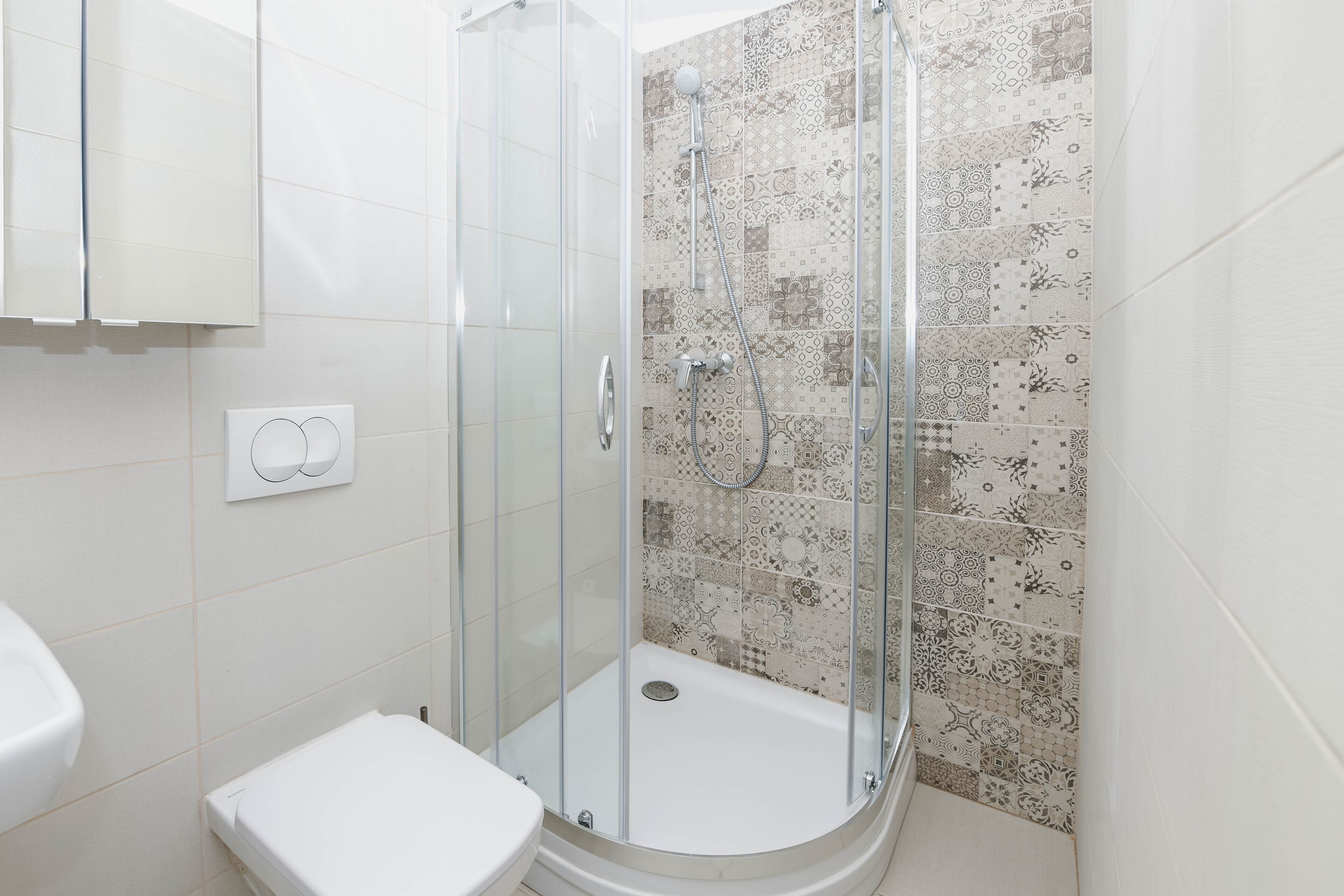 A bathroom with a glass-enclosed shower, a toilet, and patterned tiles on the walls.