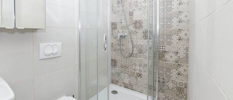 A bathroom with a glass-enclosed shower, a toilet, and patterned tiles on the walls.
