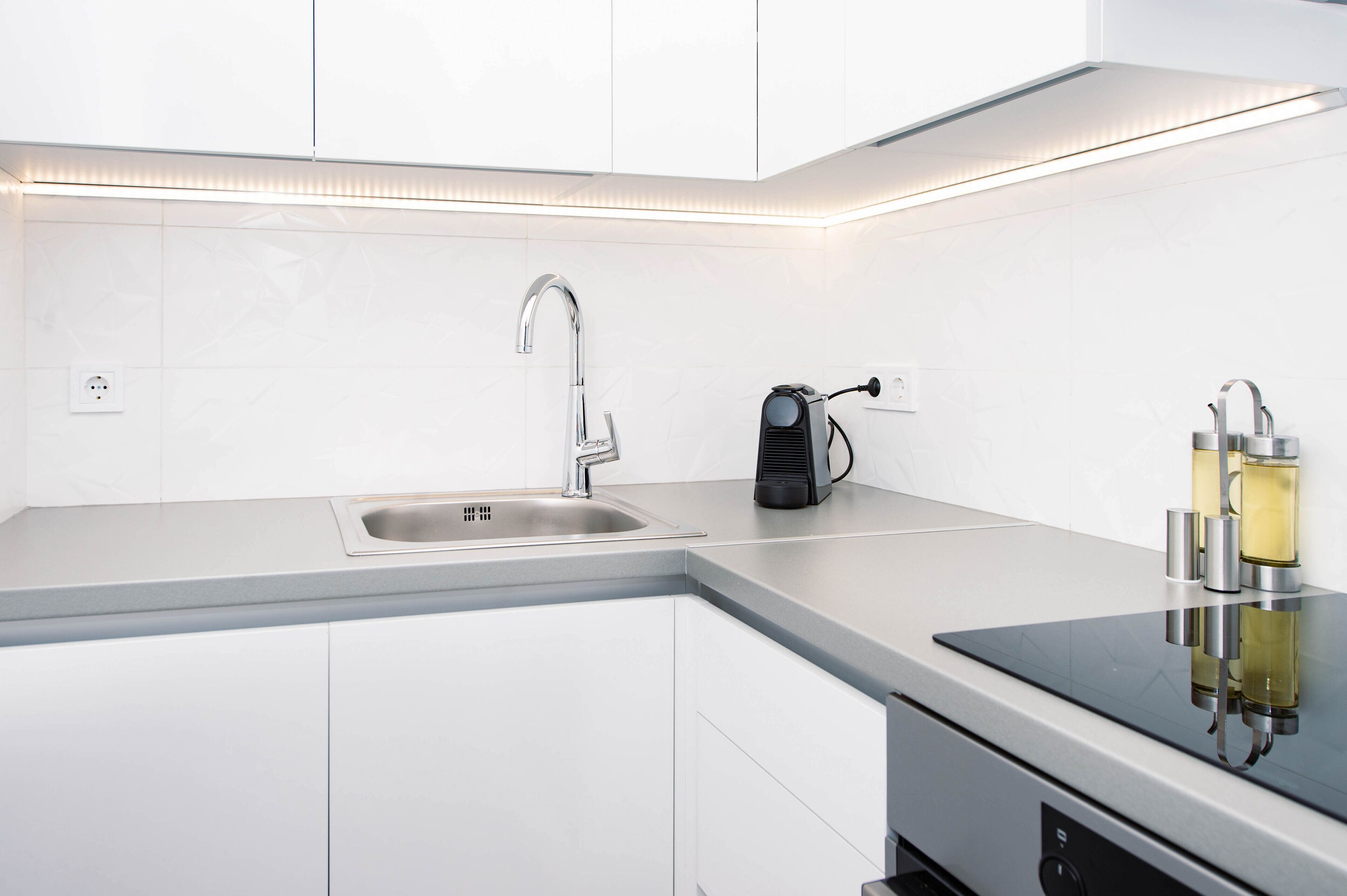 A modern kitchen with a stainless steel sink, a built-in range hood, and a black coffee maker on the countertop.