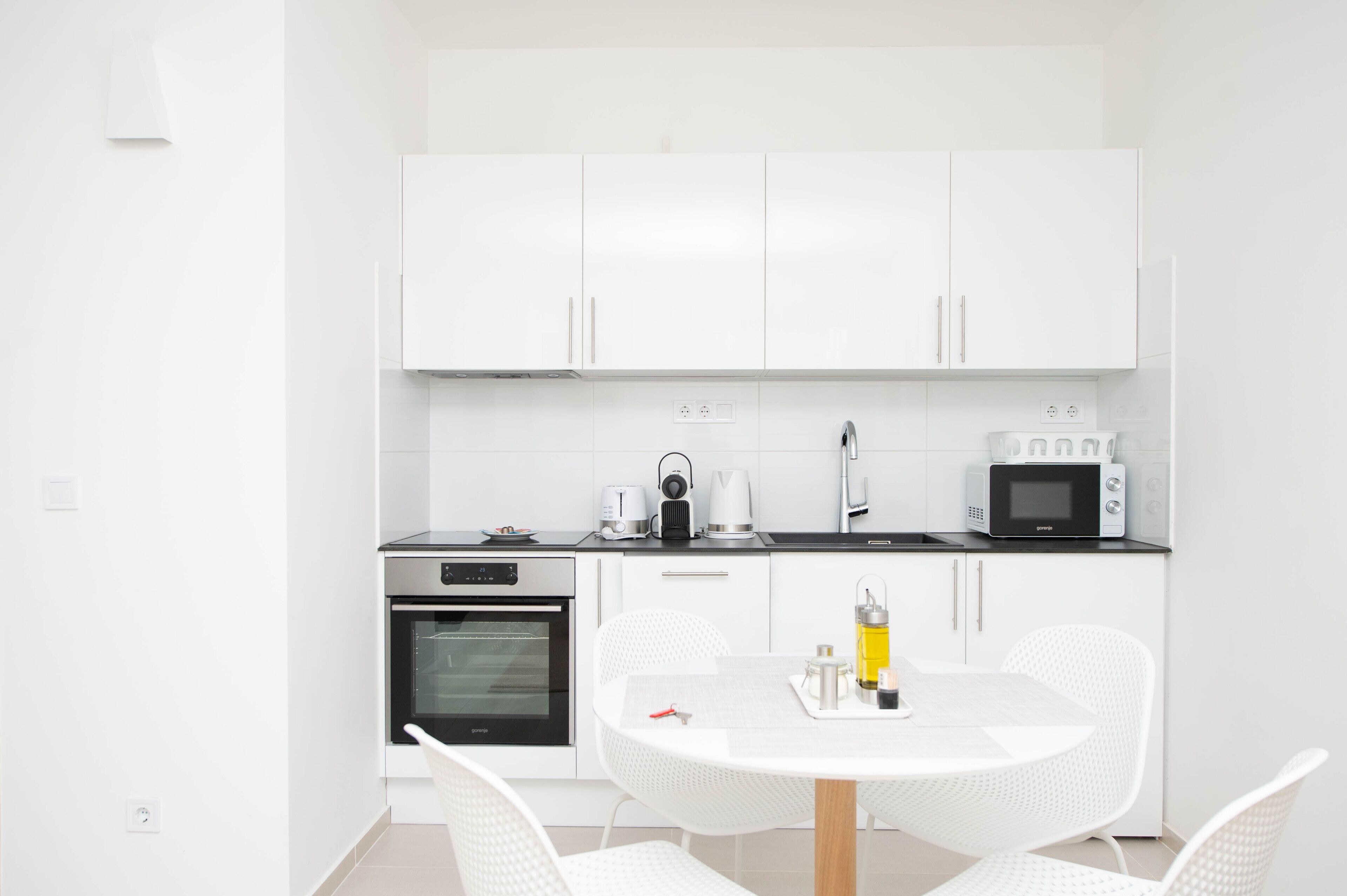 A modern kitchen with white cabinetry, a microwave, an oven, and a dining area with a white table and chairs.