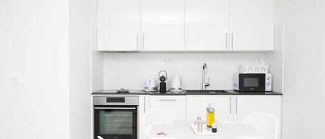 Una cocina moderna con armarios blancos, microondas, horno y comedor con mesa y sillas blancas.