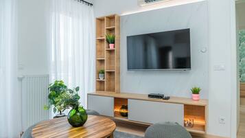 Een moderne woonkamer met een houten tv-meubel, een flatscreen televisie en een ronde houten tafel met een groene vaas.