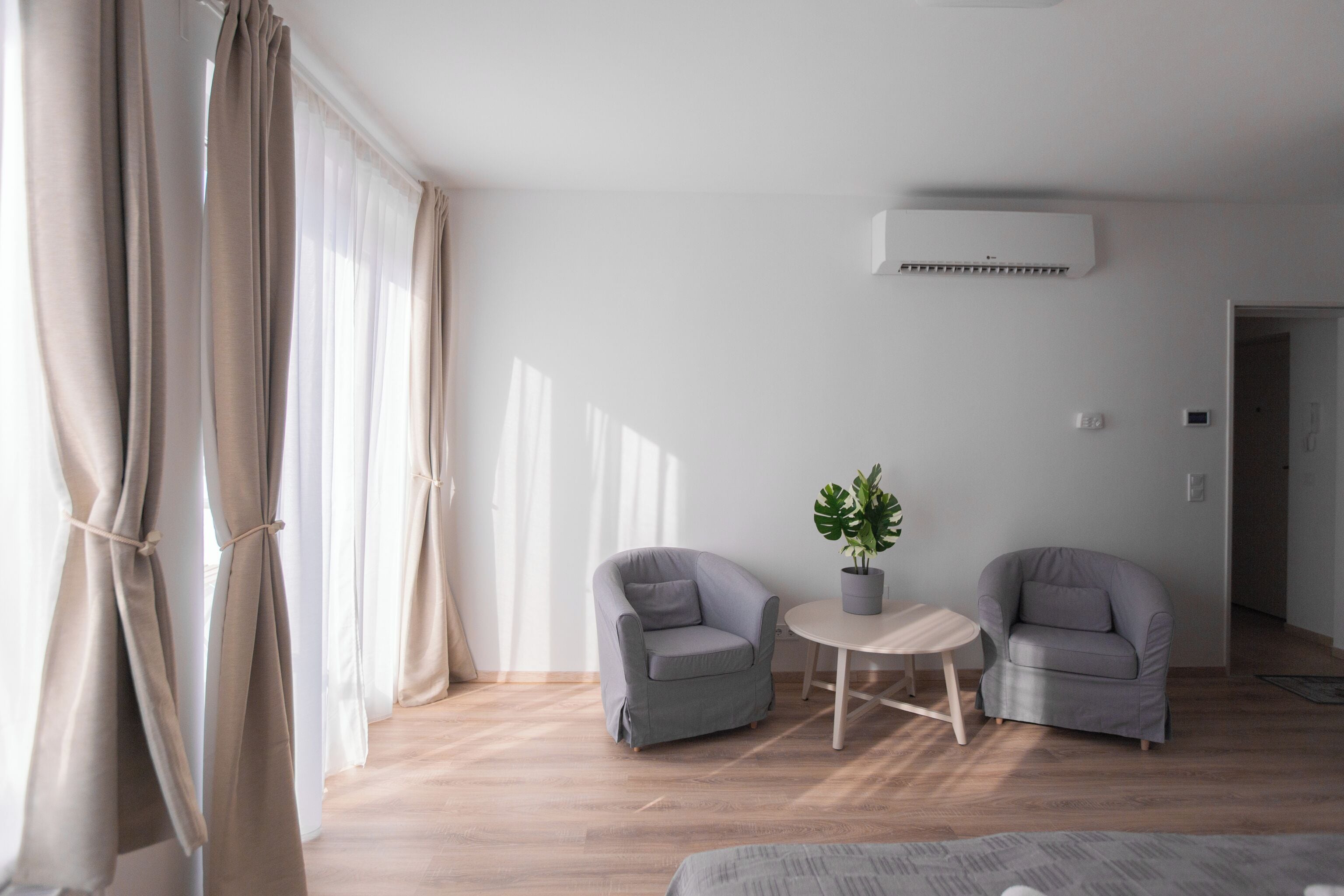 Een moderne, minimalistisch ingerichte kamer met twee grijze fauteuils, een klein rond tafeltje en een potplant.