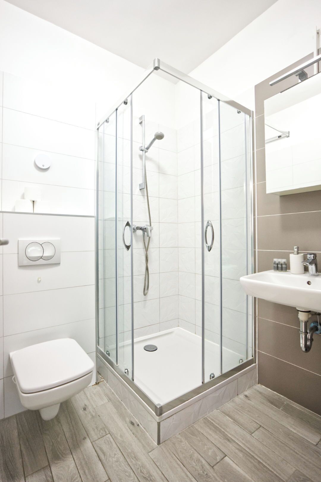 Un baño moderno con ducha de vidrio, inodoro y lavamanos con espejo.