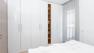 Un dormitorio con un armario grande, una pequeña estantería y una cama con ropa de cama blanca.