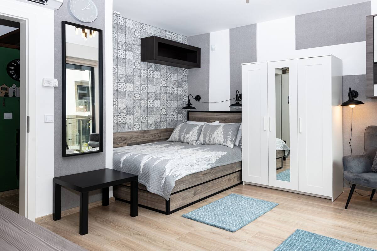 A modern bedroom with a bed, bedside table, wardrobe, and a mirror.