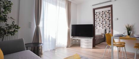 Una habitación de hotel moderna con una cama, un escritorio con computadora, un televisor y un área de comedor con sillas y una mesa.