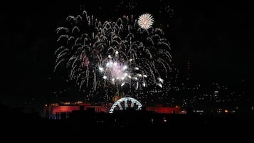 A nighttime view of a city with a prominent illuminated Ferris wheel and fireworks in the sky.