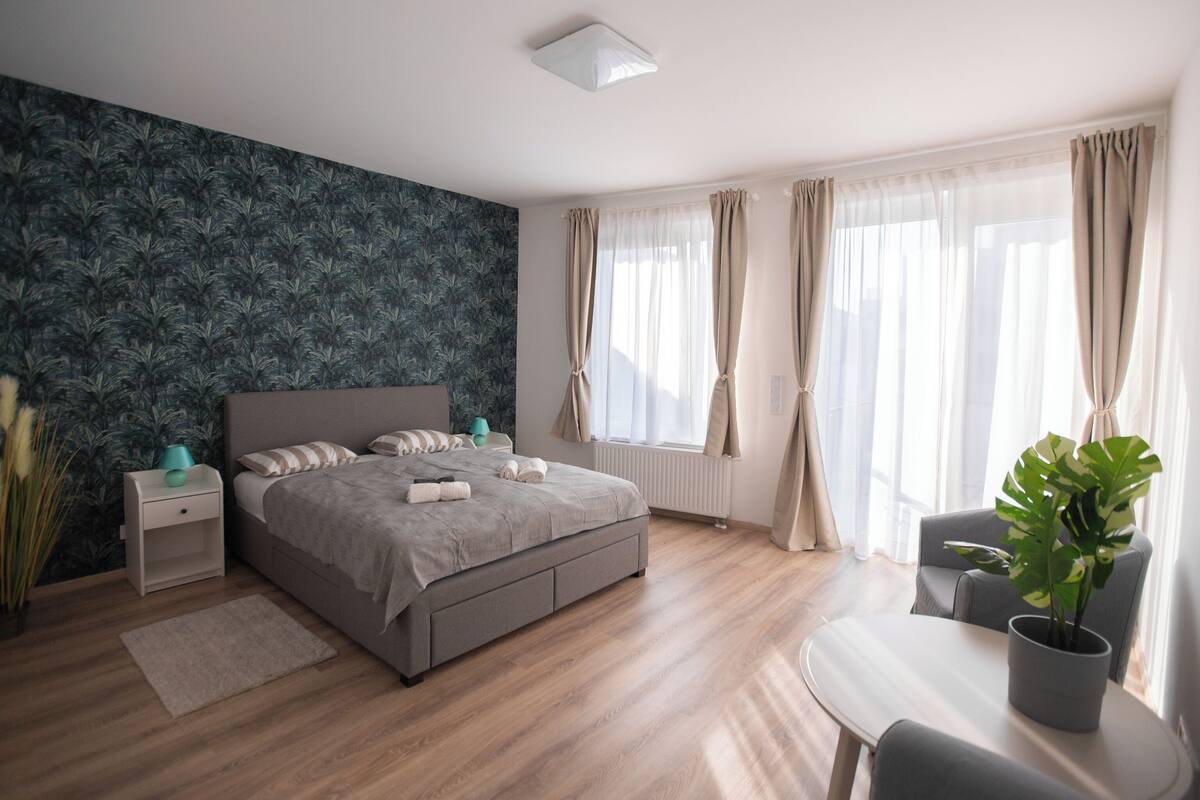 A modern bedroom with a bed, bedside tables, a desk, and a potted plant.