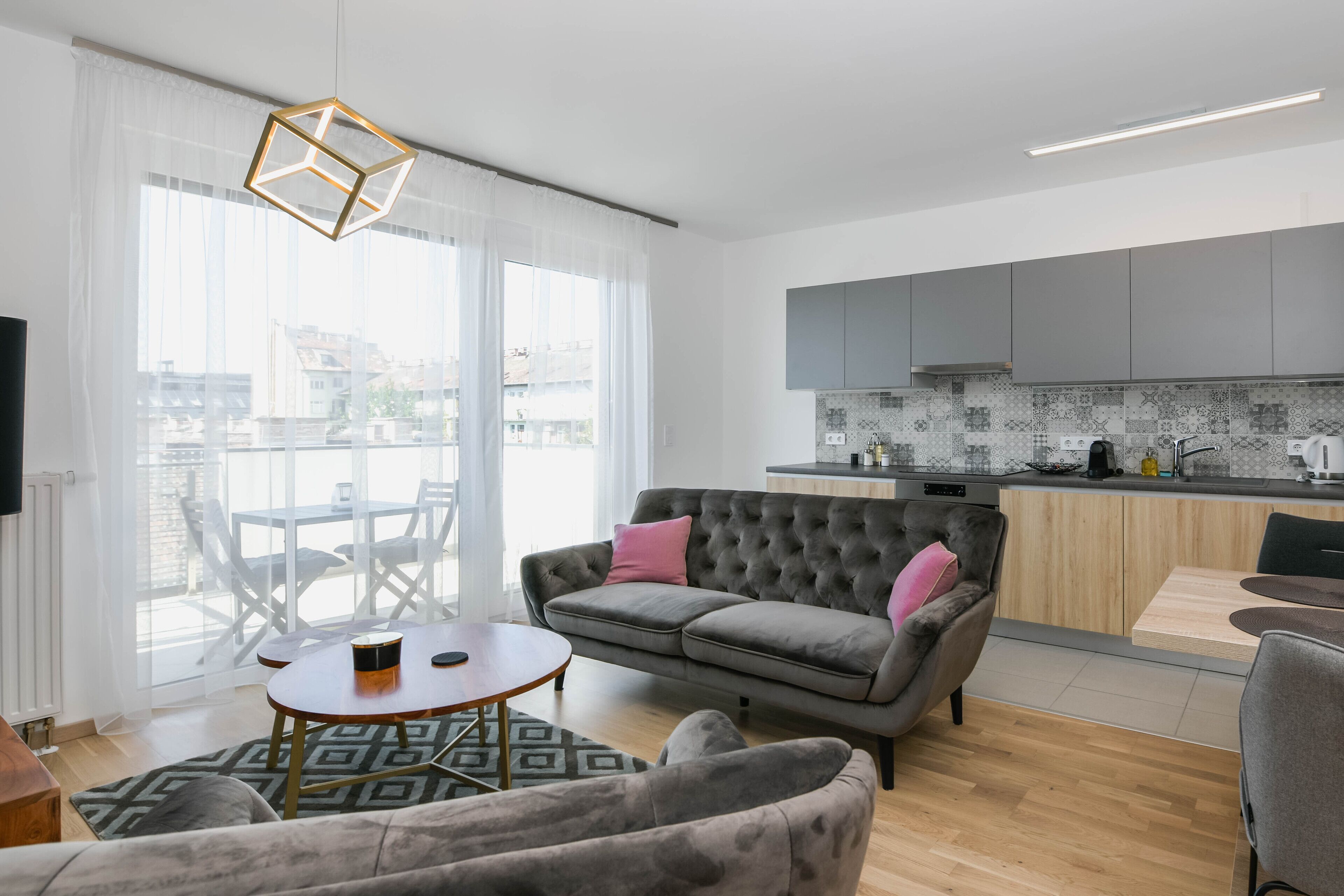 Ein modernes Wohnzimmer mit grauem Sofa, rundem Couchtisch und einem gemusterten Teppich.