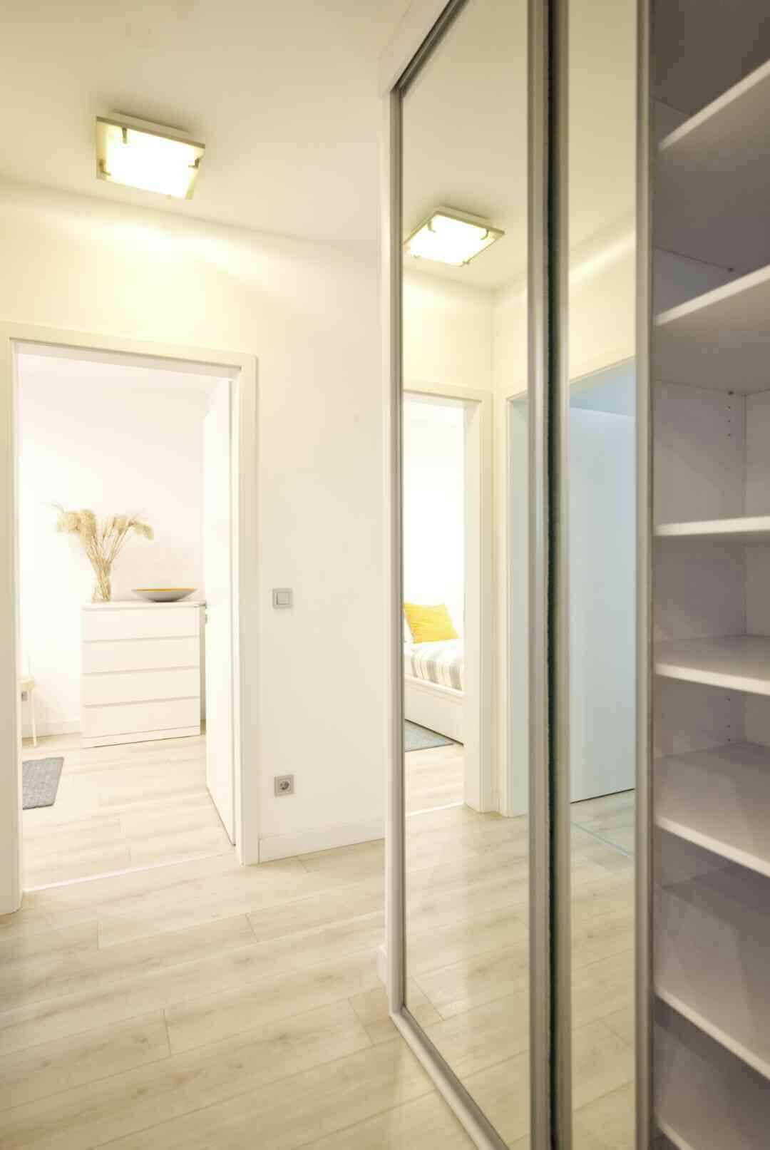 A modern, well-lit hallway with a wooden floor, a white wardrobe, and a mirrored closet door.