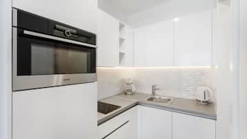 Una cucina moderna con mobili bianchi, forno integrato, macchina del caffè e bollitore.