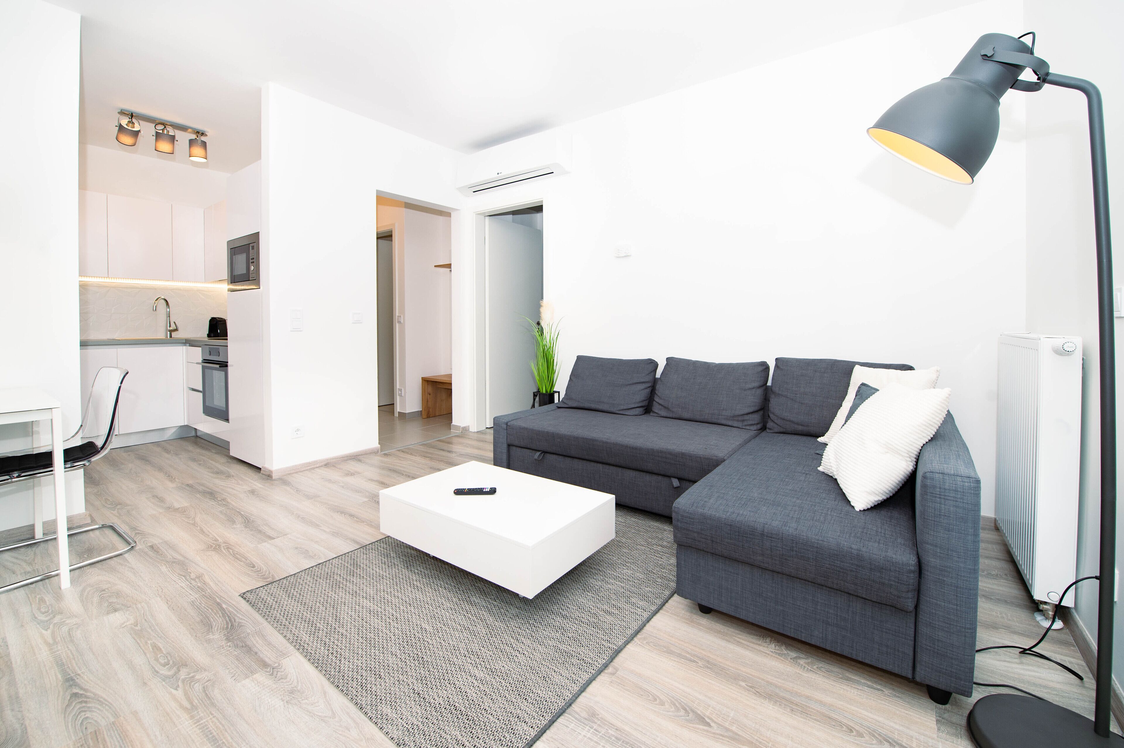 Una sala de estar moderna con un sofá gris, una mesa de centro blanca y una lámpara de pie negra.