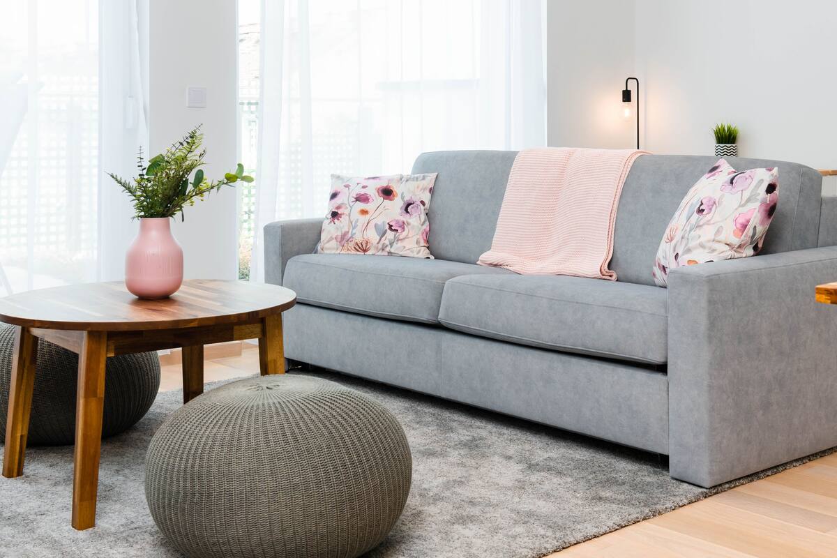 A modern living room with a grey sofa, round wooden coffee table, and two round ottomans.