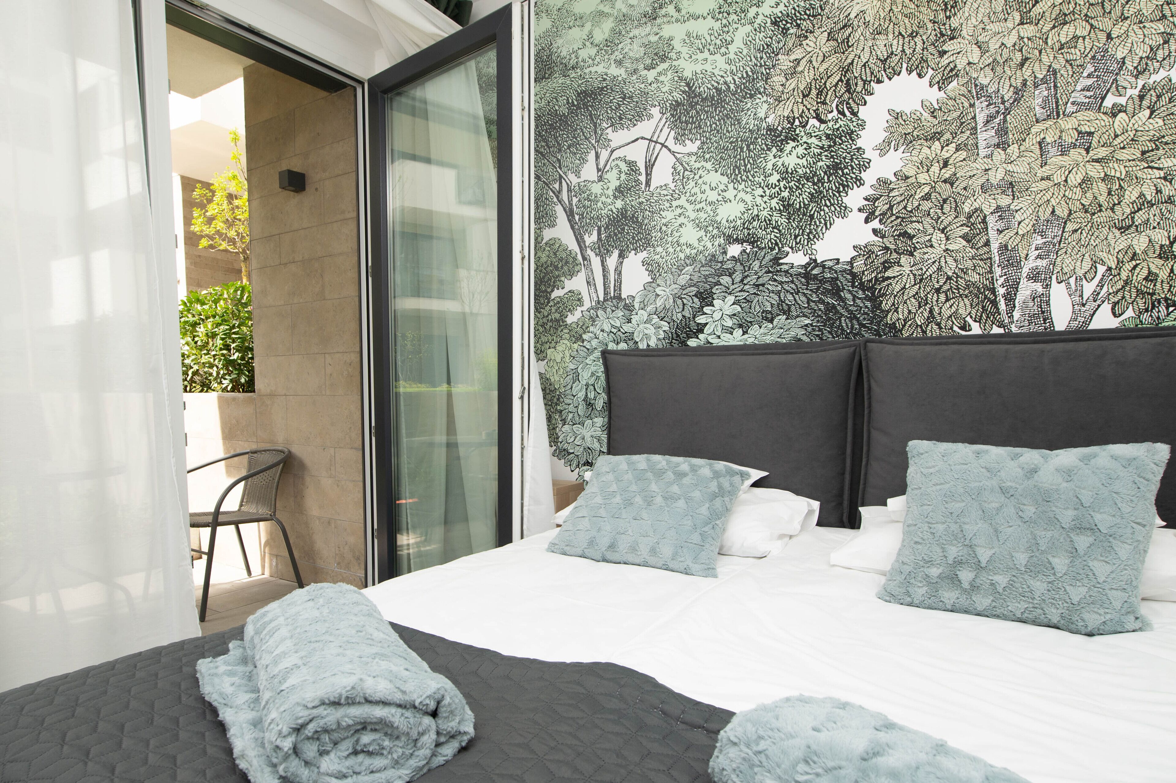 A modern bedroom with a large bed, two pillows, a dark headboard, and a glass door leading to an outdoor area.