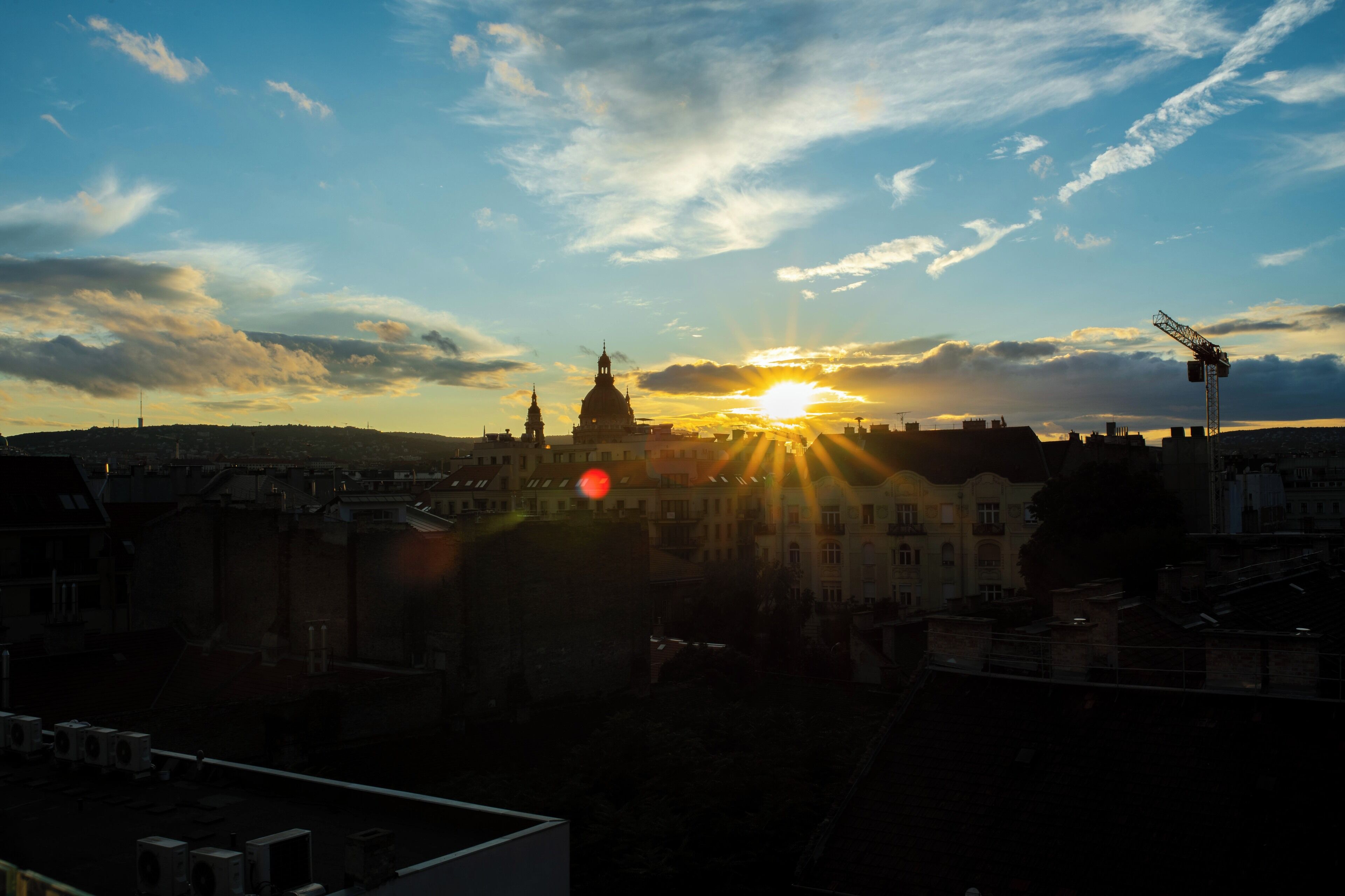A cityscape at sunset with a prominent building in the center, surrounded by various buildings and a clear sky.