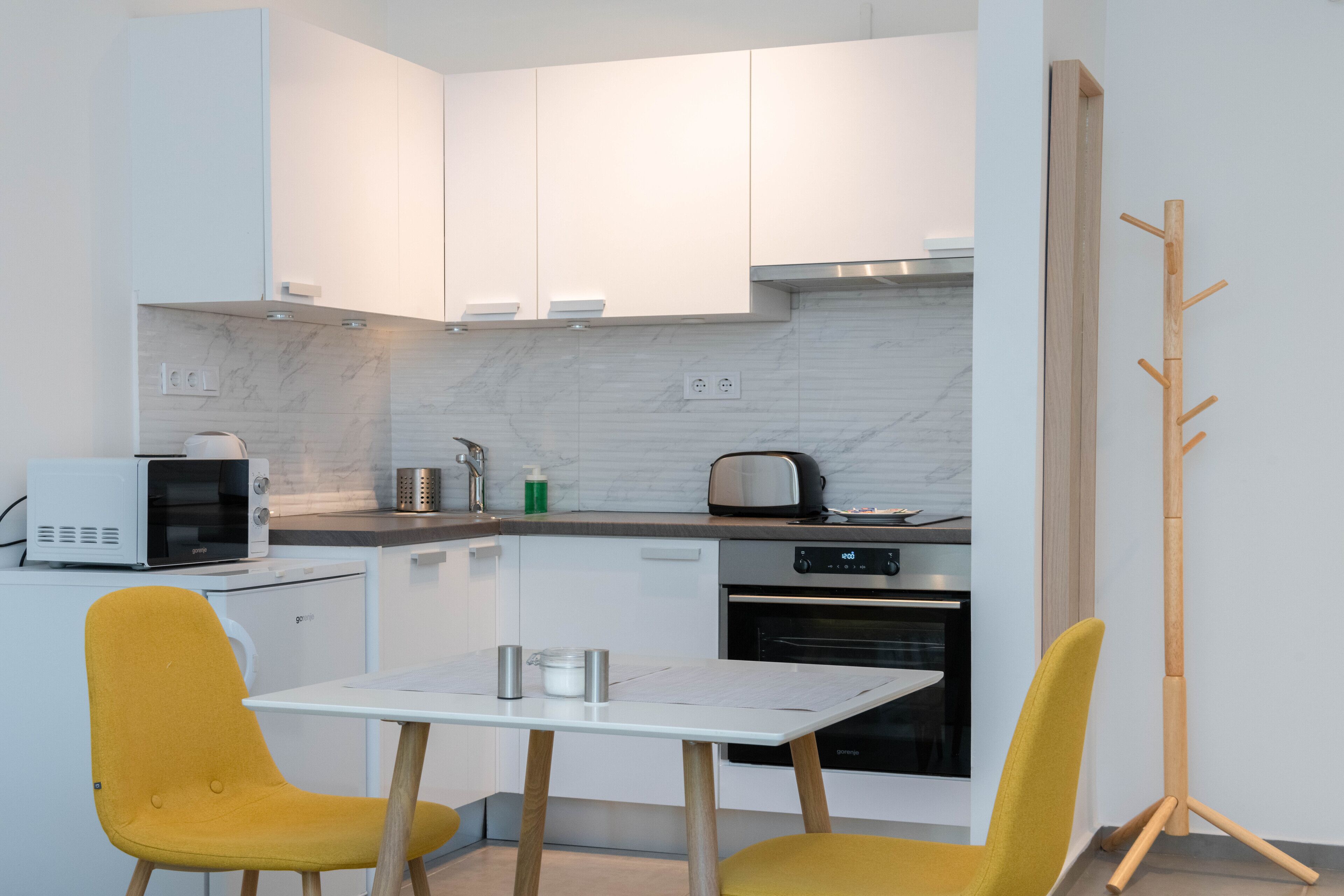 A modern kitchen with white cabinets, a microwave, toaster, and a wooden coat rack.