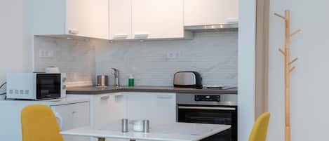 A modern kitchen with white cabinets, a microwave, toaster, and a wooden coat rack.