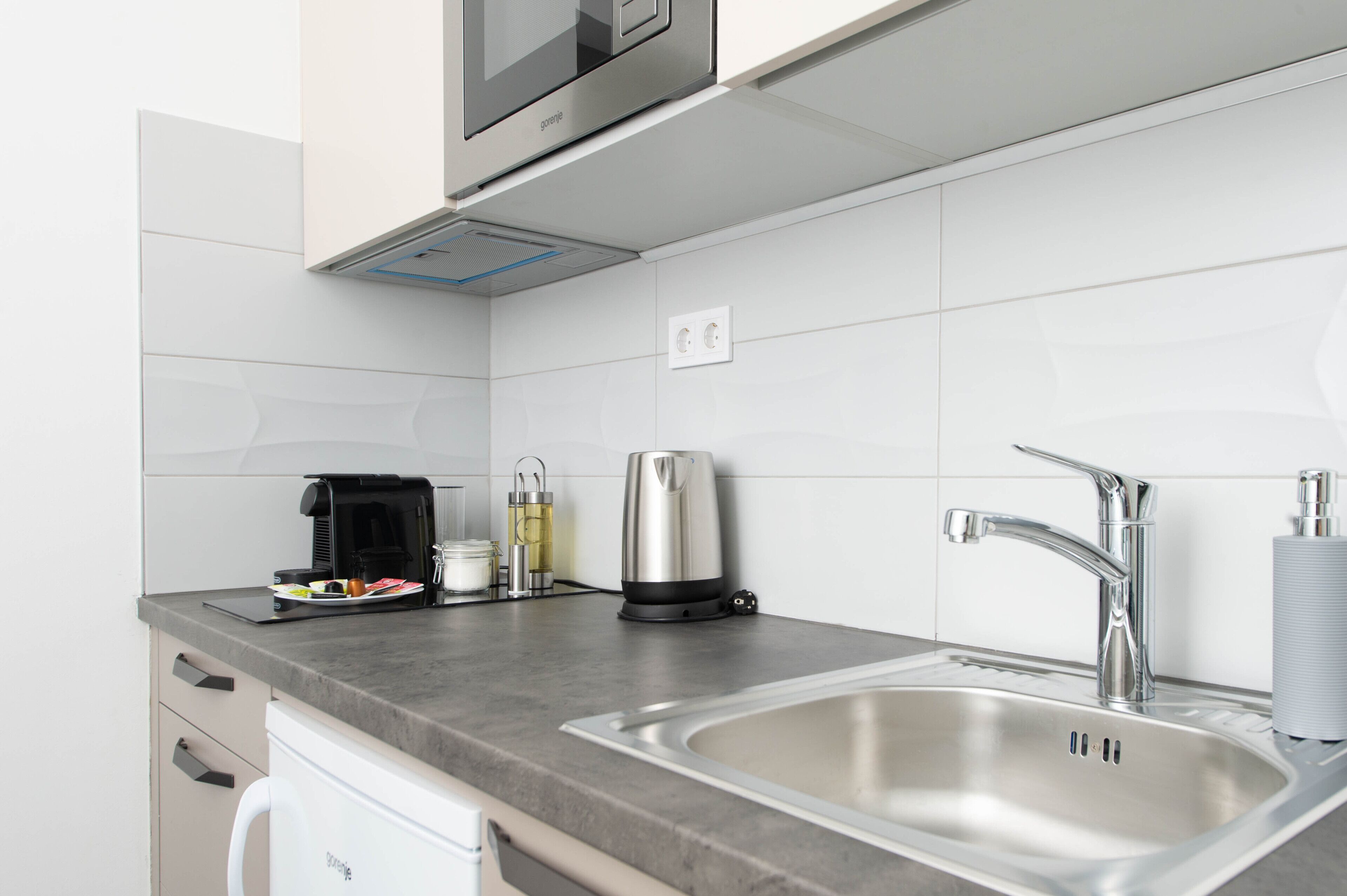 A modern kitchen with a stainless steel sink, a kettle, a coffee maker, and a microwave.