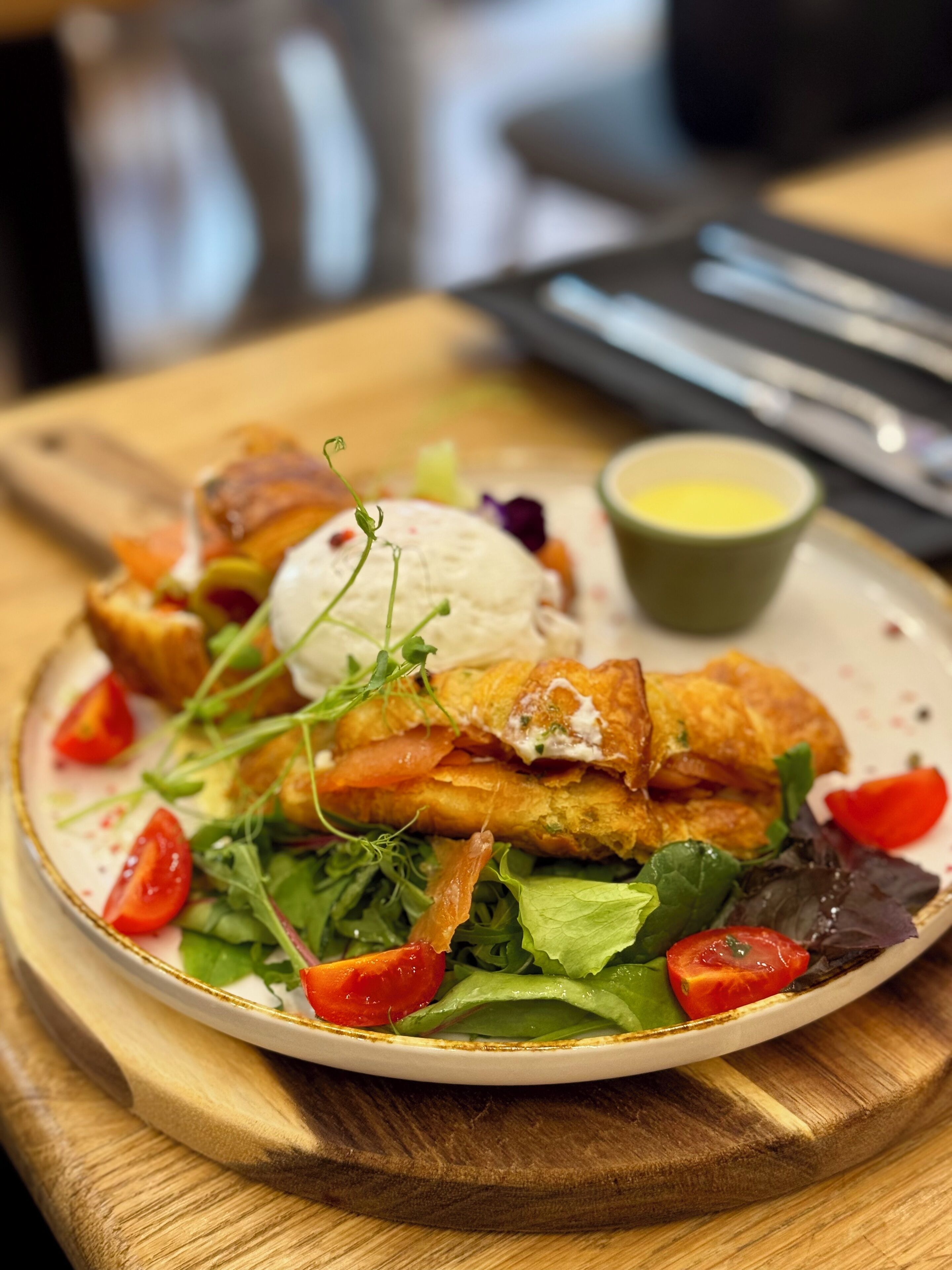 A plate of food with a salad, a poached egg, and a small bowl of sauce.