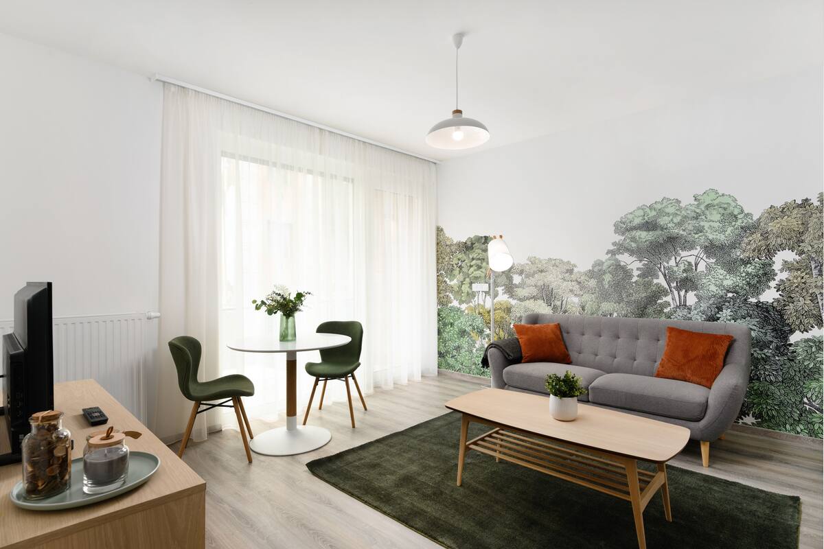 A modern living room with a grey sofa, green chairs, a wooden coffee table, and a large window with sheer curtains.