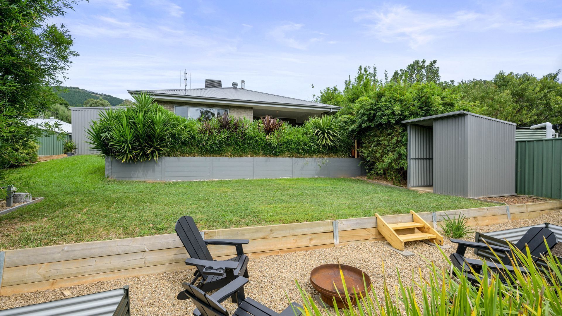Un patio trasero con una casa, una terraza de madera y un cobertizo.