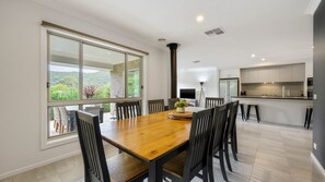 Enjoy meals in this dining area with a wooden table and six chairs, surrounded by large windows offering a view of lush greenery.
