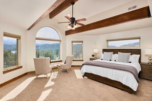 Una camera da letto con un letto grande, una ventola a soffitto, una sedia, un comodino e ampie finestre con vista sulle montagne.