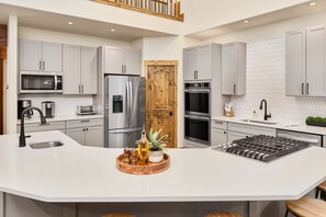 Une cuisine moderne avec des meubles gris, un îlot central, des appareils en acier inoxydable et une porte en bois.