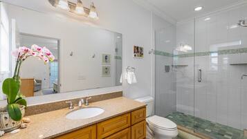 Een moderne badkamer met een wastafel met granieten blad, houten kastjes, een wit toilet en een douchecabine met glazen wanden.