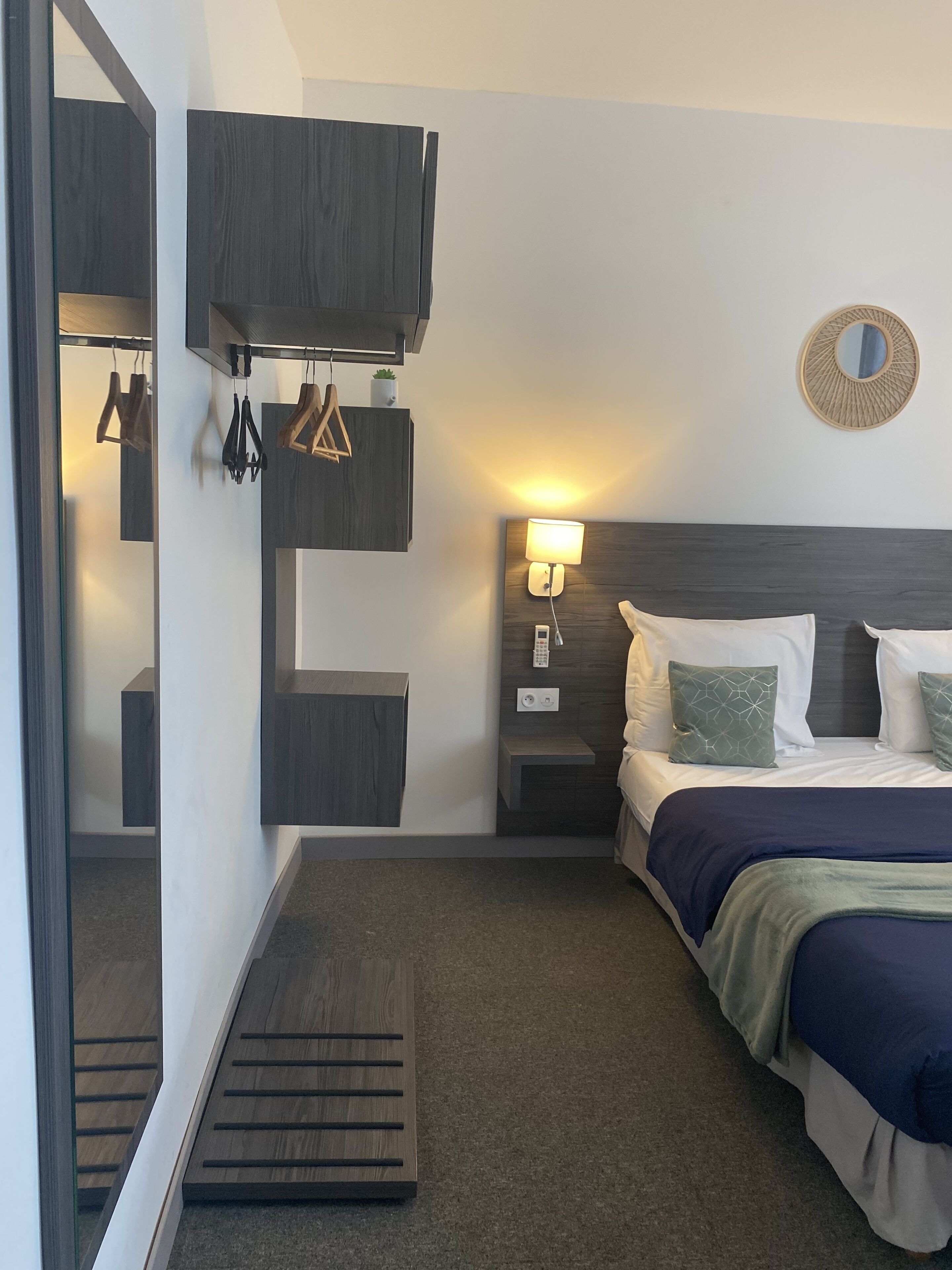 A modern hotel room with a bed, bedside table, lamp, and a mirror.