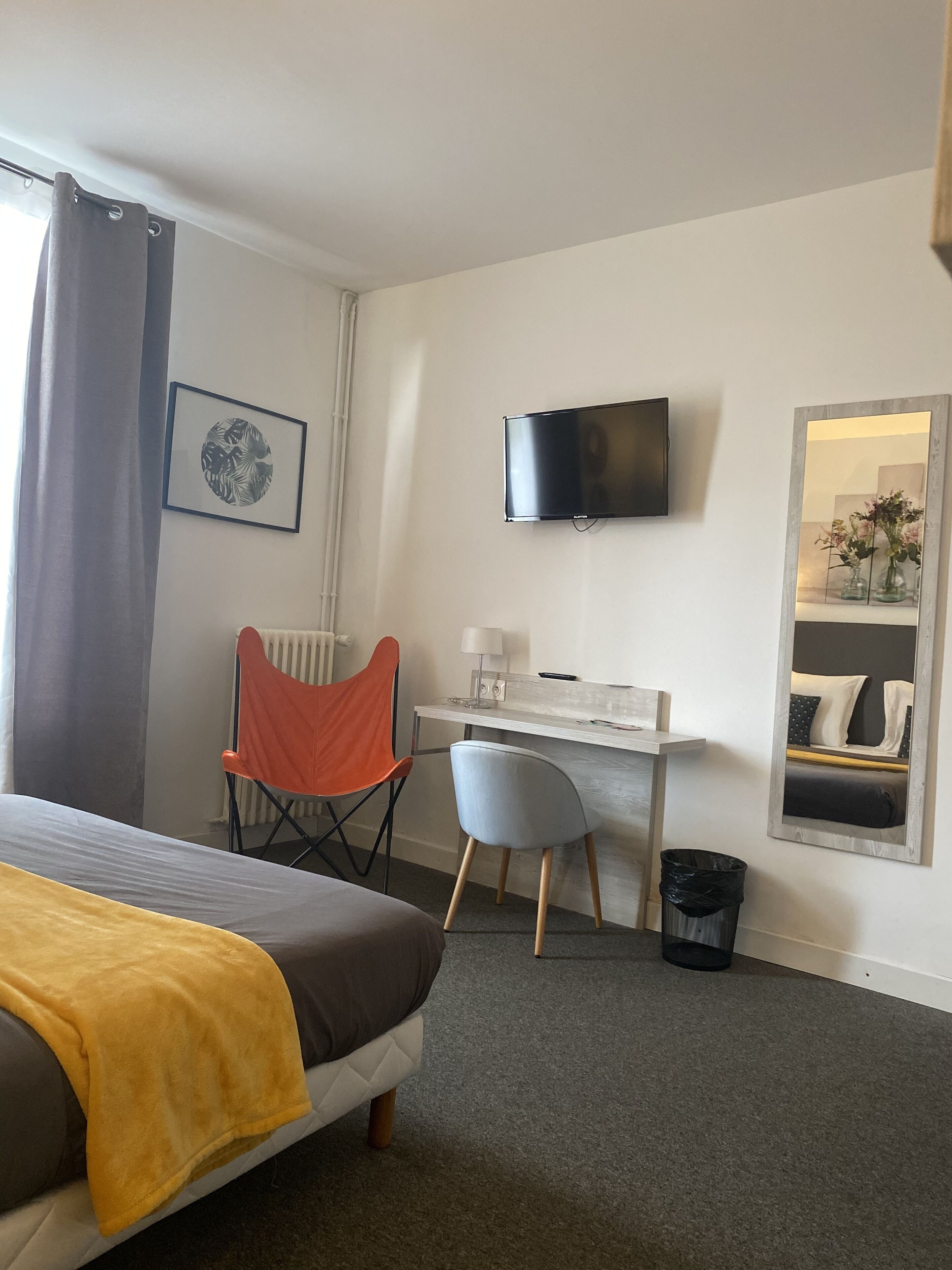 A hotel room with a bed, a desk, a chair, a television, and a mirror.