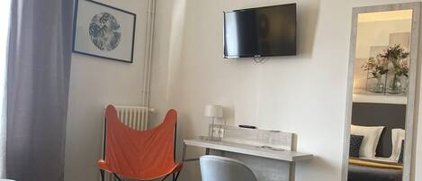 A hotel room with a bed, a desk, a chair, a television, and a mirror.