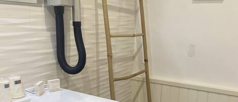 A bathroom with a wooden vanity, a white sink, a towel rack, a towel dispenser, a ladder, and a wire basket.