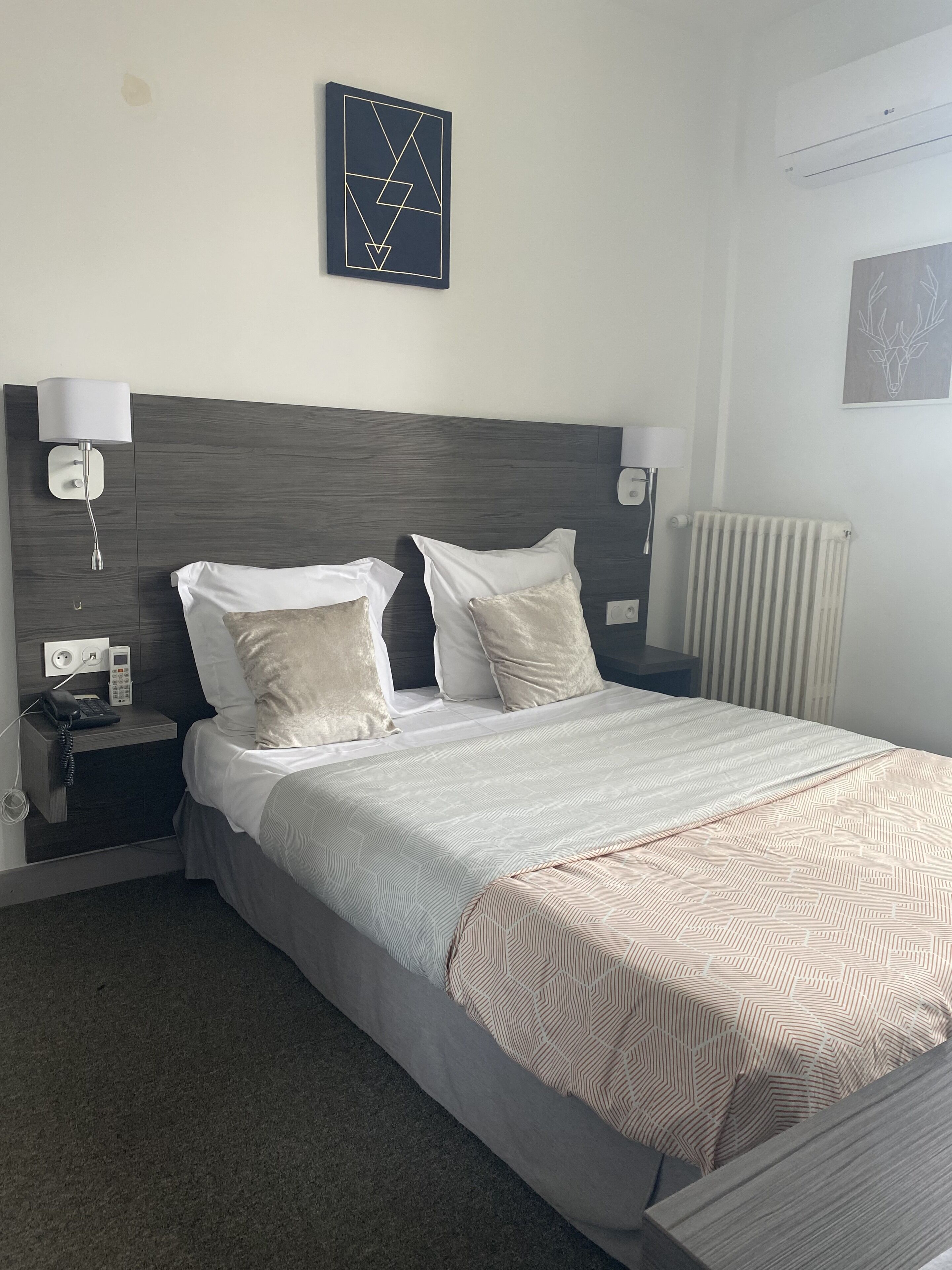 A neatly arranged hotel room with a large bed, two bedside tables, a wall-mounted artwork, and a radiator.