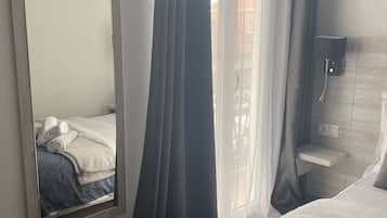 A bedroom with a large mirror, a bed with a blue and white duvet, a bedside table, and a wall-mounted lamp.