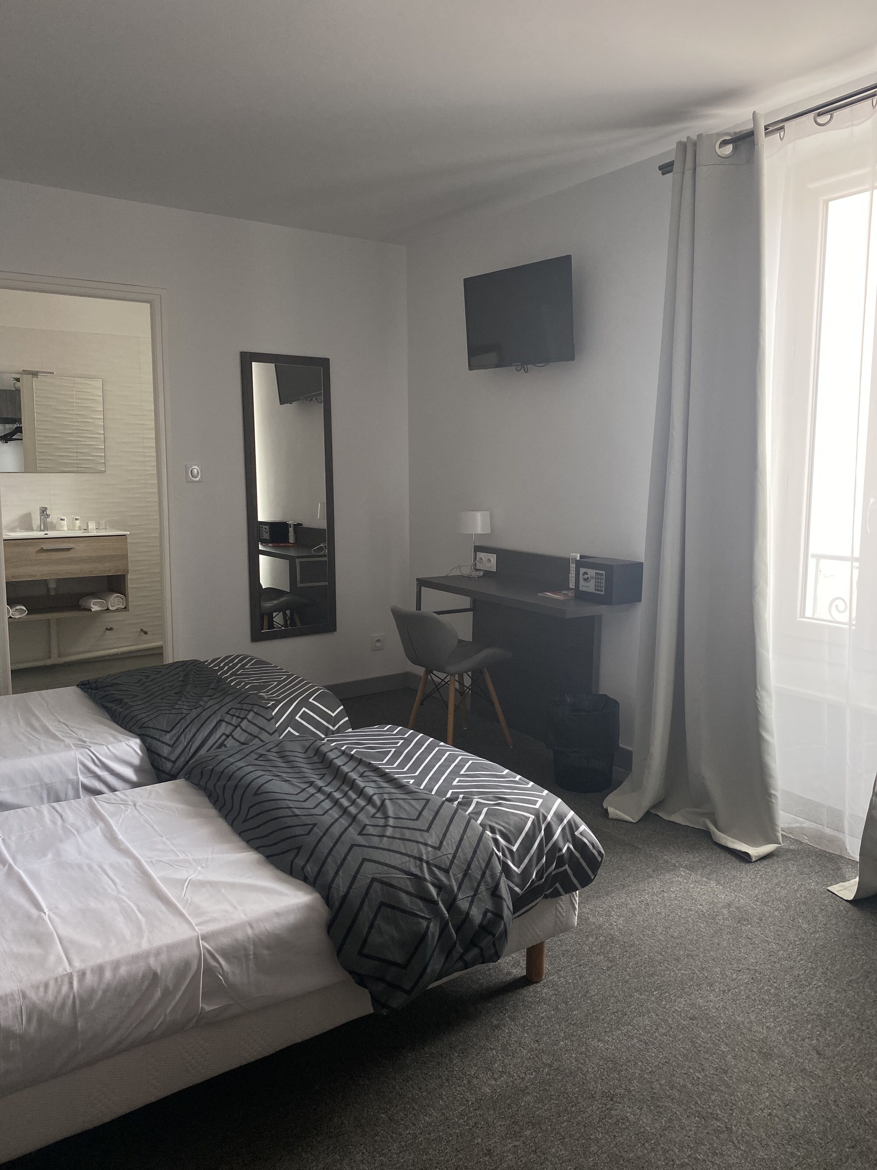 Une chambre d’hôtel avec un lit, un bureau, une chaise, une télévision et une salle de bain visible à travers une porte ouverte.