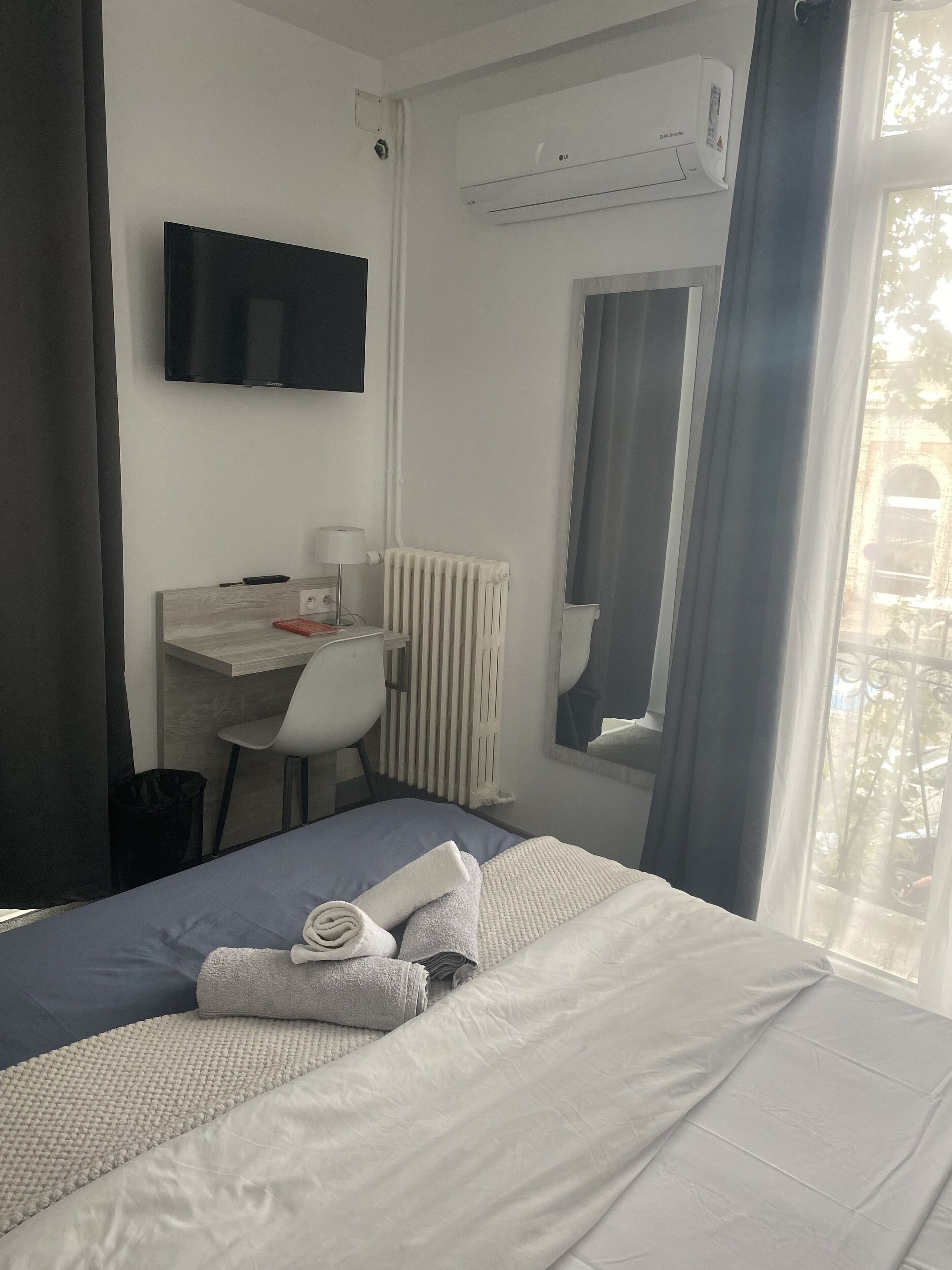 A hotel room with a bed, a desk, a chair, a TV, and an air conditioning unit.