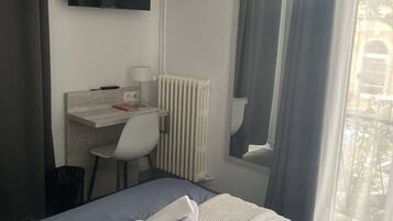 A hotel room with a bed, a desk, a chair, a TV, and an air conditioning unit.