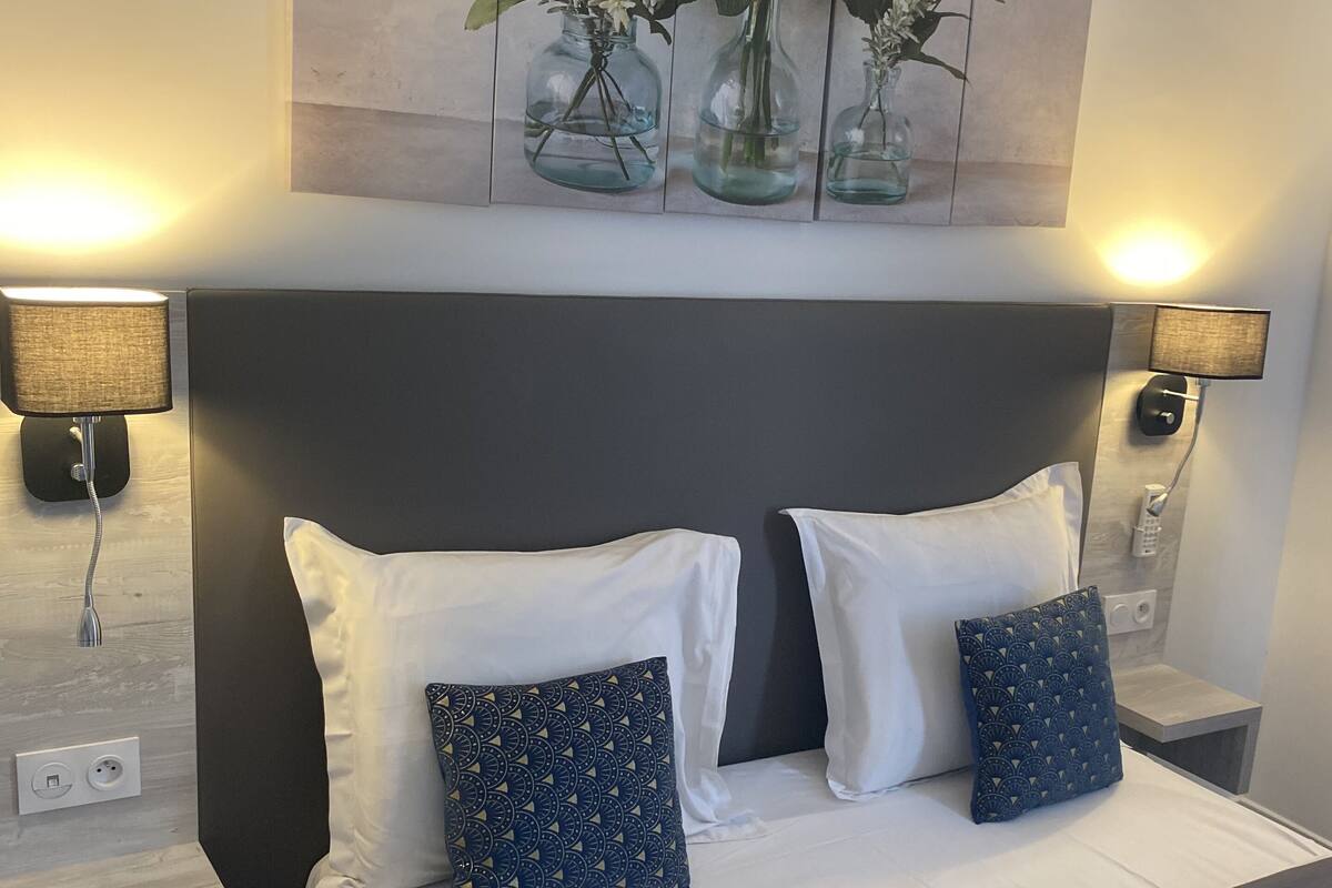 A hotel room with a large bed, two nightstands, two lamps, and a painting of vases with flowers on the wall.