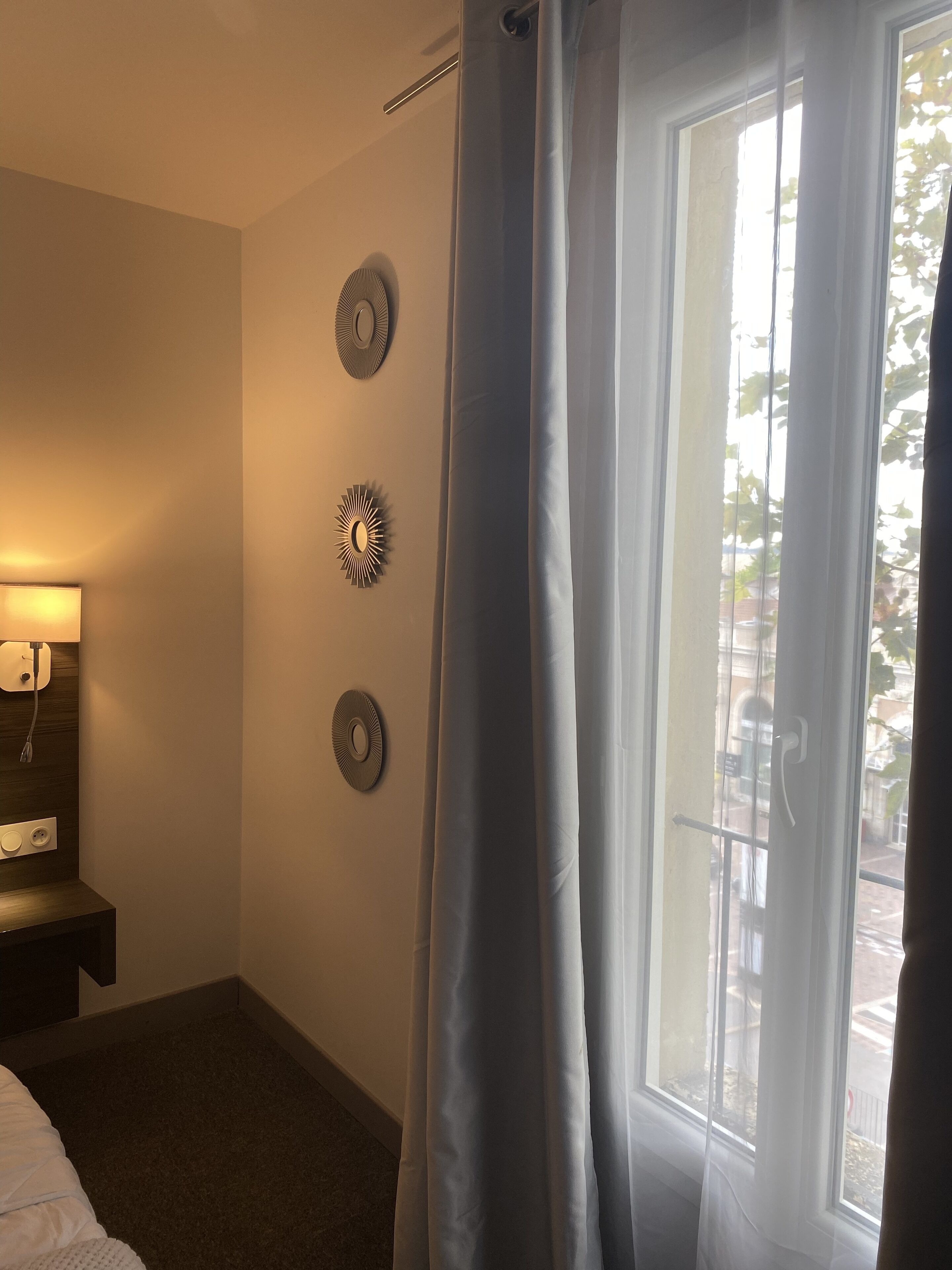 Habitación de hotel con cama, mesita de noche con lámpara, ventana con cortinas y decoración en la pared.